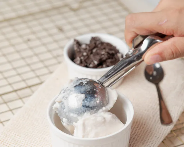 A metal scoop lifting vanilla ice cream from a white ramekin.