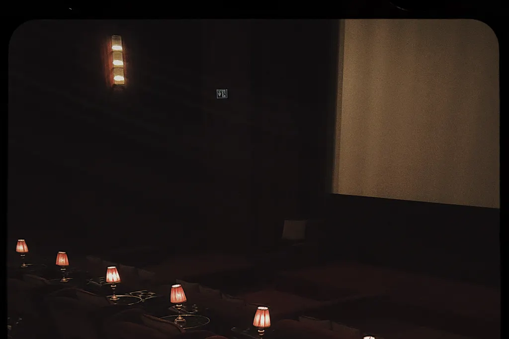 A small dark screening room with low tables, each lit by a little red lamp.