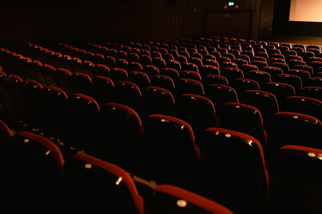 Rows of worn red velvet seats in a dim auditorium, lit from the side.