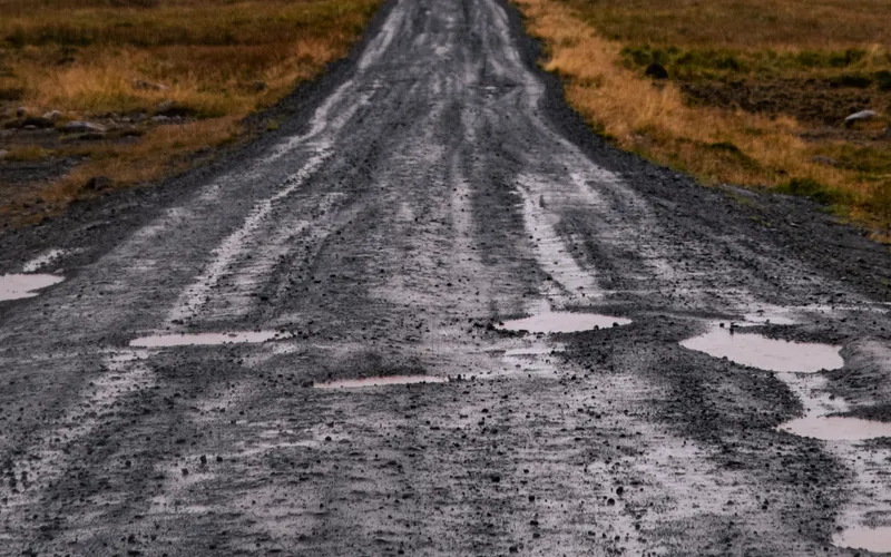A muddy rural track full of rain puddles running straight to the horizon.