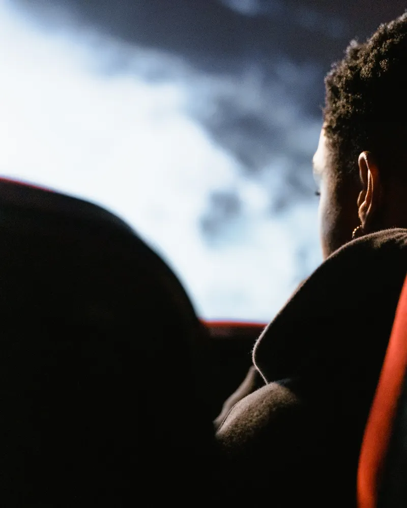 A man in a red velvet seat watches the screen, lit only by its glow.
